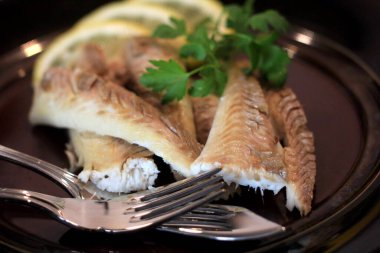 Koyu bir tabakta, limonla süslenmiş balık filetosu. Tuzda pişmiş balık. 