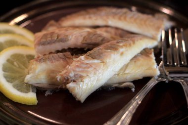 Koyu bir tabakta, limonla süslenmiş balık filetosu. Tuzda pişmiş balık. 