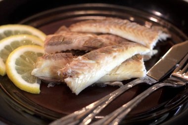 Koyu bir tabakta, limonla süslenmiş balık filetosu. Tuzda pişmiş balık. 