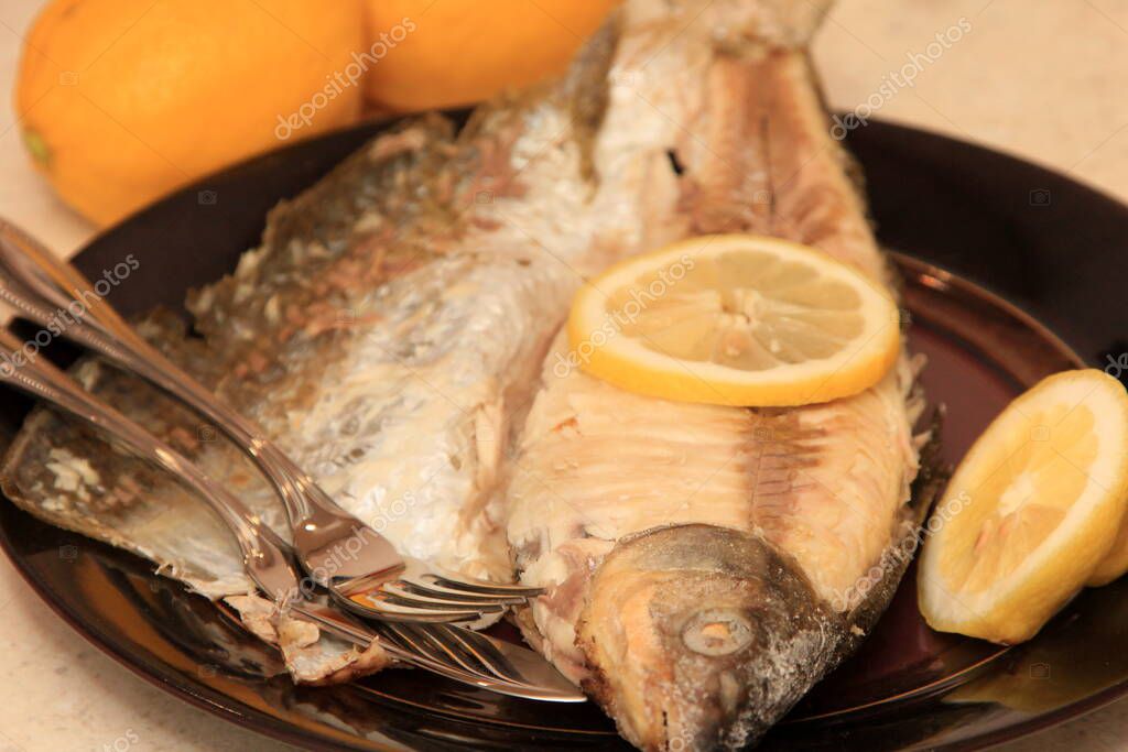 Pescado frito entero en un plato oscuro, decorado con limón. Pescado