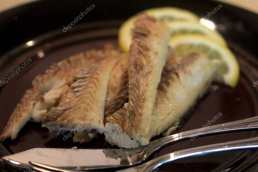 Filete de pescado cocido en un plato oscuro, decorado con limón