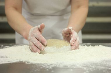 Kadının elleri ekmek hamurunu yoğuruyor. Ahşap masada kadın elleriyle para kazanıyorlar.