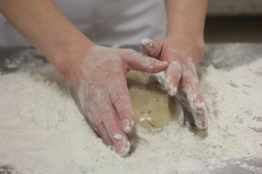 Kadının elleri ekmek hamurunu yoğuruyor. Ahşap masada kadın elleriyle para kazanıyorlar.