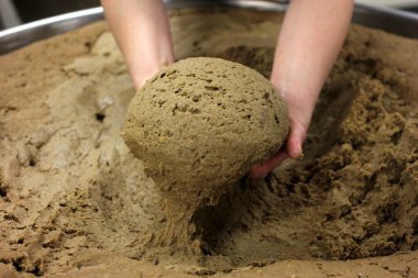 Ev yapımı ekmek hamuru. Elle yapılmış ve büyük bir tencere şeklinde. Kadının elleri ekmek hamurunu yoğuruyor..