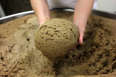 Ev yapımı ekmek hamuru. Elle yapılmış ve büyük bir tencere şeklinde. Kadının elleri ekmek hamurunu yoğuruyor..