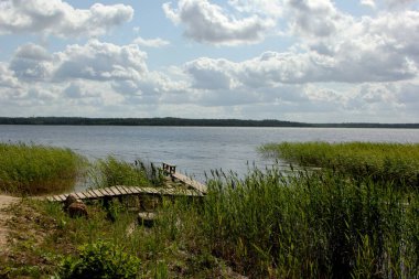 Yeşil tepeli göl, güneşli yaz günü gökyüzünde bulutlar Letonya 'da Usma Gölü. Göldeki tahta köprüler. 