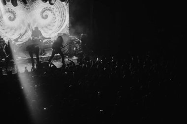 Bir metal grubunun canlı performansı sırasında siyah-beyaz bir kulübün sahnesinde kalabalık tezahürat yapıyor..