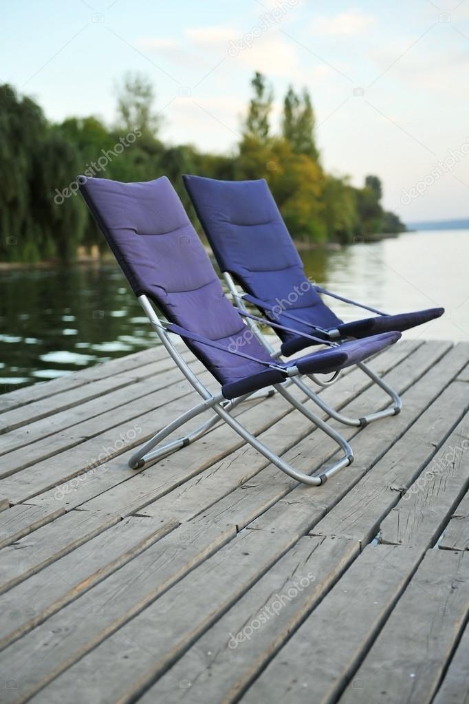 Two blue folding chairs on a wooden platform on the river