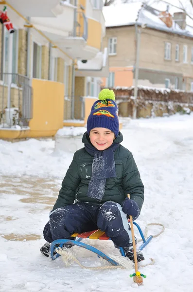 Little boy sitting on a sled in the yard of a house. — Stock Photo, Image