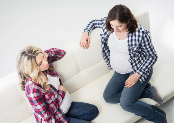 Zwei schwangere Freundinnen plaudern auf dem Sofa — Stockfoto