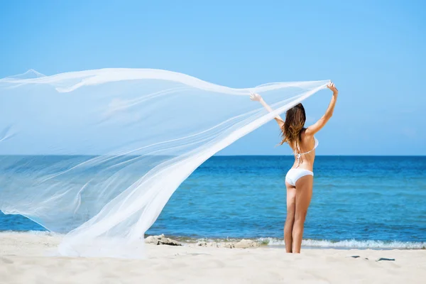 Ung kvinna poserar med blåser silk på stranden — Stockfoto