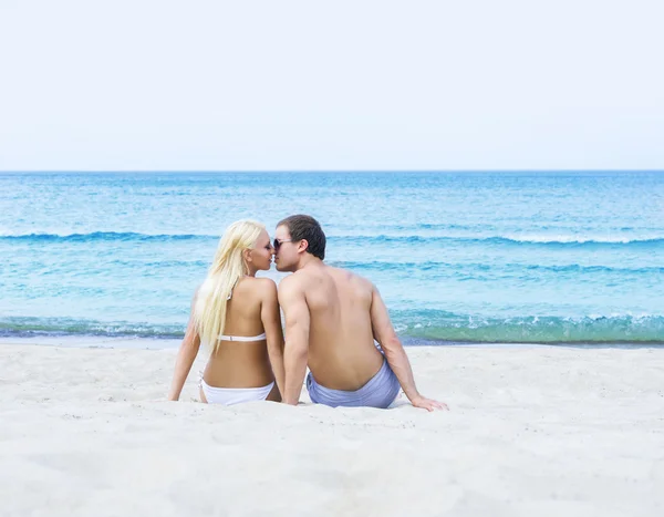 Hombre y mujer sentados y besándose en una playa de verano — Foto de Stock