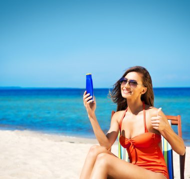 Kumsalda güneş losyonu tutan genç kadın