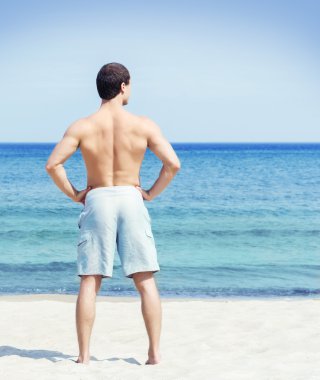 Genç bir adam sahilde poz arkası