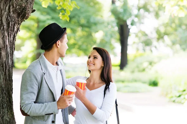 一緒にコーヒーを飲みながら公園を歩く若いカップル — ストック写真