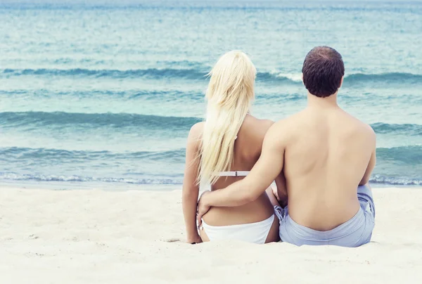 Hombre y mujer en trajes de baño sentados y abrazados en la playa —  Fotos de Stock
