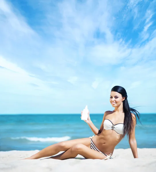 Mulher jovem e sexy segurando uma garrafa de protetor solar na praia — Fotografia de Stock