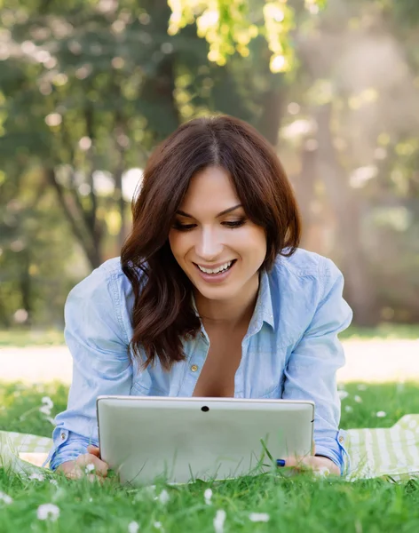 Fröhliche, junge Frau blättert im Park mit ihrem Tablet — Stockfoto