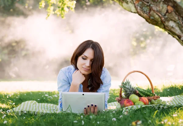 Young brunette surfing the web  in the park on a misty backgroun — Stock Photo, Image