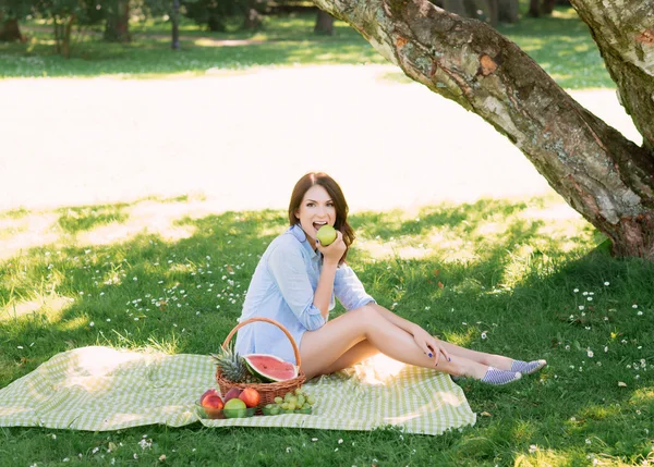 Hermosa morena joven comiendo una manzana en el parque —  Fotos de Stock