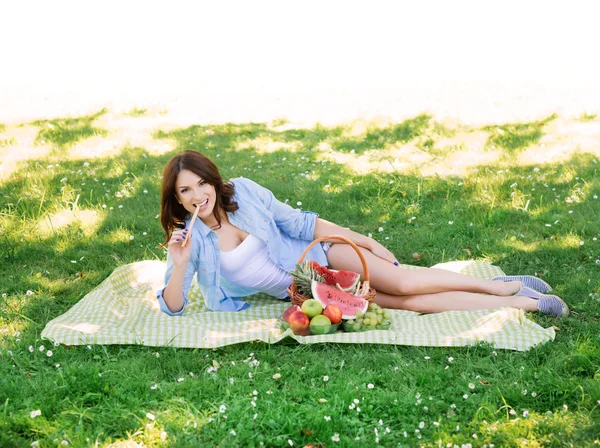 Prachtige brunette liggen op een mat en eten in het park. — Stockfoto