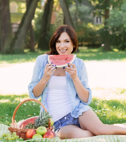 Mujer joven sentada en el parque y comiendo una sandía . Fotos de stock