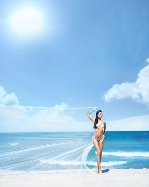 Mujer joven y en forma posando con seda soplando en una playa de verano —  Fotos de Stock