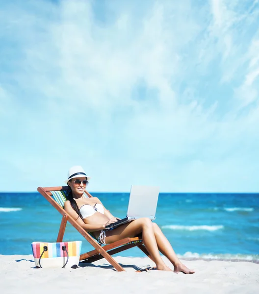 Menina sexy em uma espreguiçadeira trabalhando com um laptop na praia Fotografias De Stock Royalty-Free