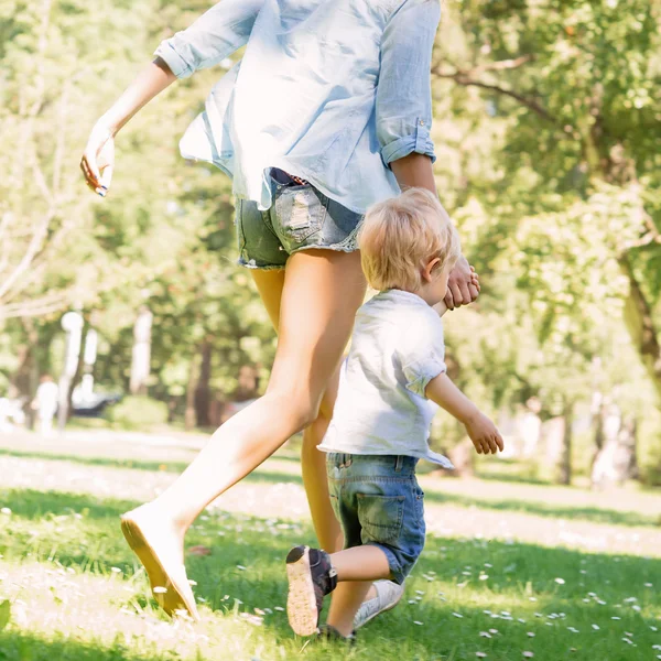 Genç anne parkta yürümeye başlayan çocuk oğluyla yürüyüşe sahip — Stok fotoğraf