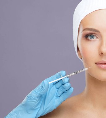 Genç bir kadının güzel yüzüne iğne yapan bir doktor. Estetik ameliyat, cilt gerdirme ve estetik tıp konsepti.