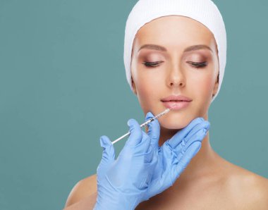 Genç bir kadının güzel yüzüne iğne yapan bir doktor. Estetik ameliyat, cilt gerdirme ve estetik tıp konsepti.