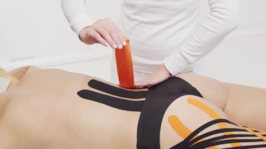 Terapist kadın vücuduna kinesio bandı uyguluyor. Fizyoterapi, kineziyoloji ve iyileşme tedavisi kavramları.