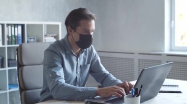 İşadamı bilgisayar teknolojisini kullanarak modern ofiste tek başına çalışıyor. Koruyucu maskeli adam. Genç ve kendinden emin iş adamının işyeri..