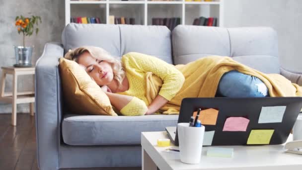 仕事に疲れたフリーランスの女の子は朝ソファの上で眠る 家で働いている間に若い女性は眠ってしまった ロックダウンとリモートジョブの概念 — ストック動画