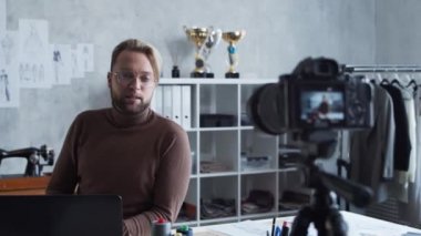 Genç moda blogcusu kamera kullanarak kıyafet tasarımı hakkında video blogu kaydediyor. Modern çatı katındaki iş yerinden yetenekli stilist akışı..