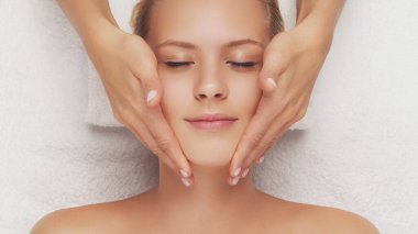 Genç, güzel ve sağlıklı bir kadın masaj salonunda. Geleneksel yüz masajı terapisi ve cilt bakımı.