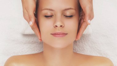 Genç, güzel ve sağlıklı bir kadın masaj salonunda. Geleneksel yüz masajı terapisi ve cilt bakımı.