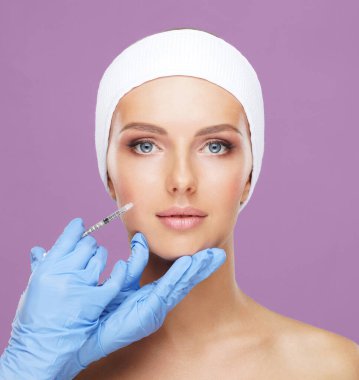 Genç bir kadının güzel yüzüne iğne yapan bir doktor. Estetik ameliyat, cilt gerdirme ve estetik tıp konsepti.