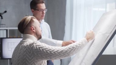 Mimar ve meslektaşı çizim tahtasını kullanarak çatı katında çalışıyorlar. Modern ofisteki genç mühendisin işyeri. Gayrimenkul geliştirme kavramı.