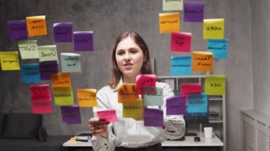 Genç iş kadını camdaki çıkartmaları kullanarak beyin fırtınası yapıyor. Ofis çalışanı strateji, iş planı ve hedefleri düşünüyor. Başlangıç konsepti.