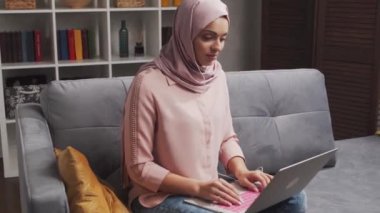 Genç ve çekici tesettürlü Müslüman kadın evde dizüstü bilgisayar kullanıyor. Orta Doğulu serbest çalışan ya da kanepede yatan bir öğrenci. Kilitleme kavramı.