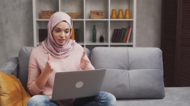 Genç ve çekici tesettürlü Müslüman kadın evde dizüstü bilgisayar kullanıyor. Orta Doğulu serbest çalışan ya da kanepede yatan bir öğrenci. Kilitleme kavramı.