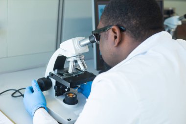 Laboratuvarda çalışan Afrikalı-Amerikalı bilim adamı. Erkek doktor mikrobiyoloji araştırması yapıyor. Laboratuvar aletleri: mikroskop, test tüpleri, ekipmanlar. Biyoteknoloji, kimya, bakteriyoloji, viroloji, DNA ve