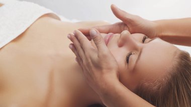Genç, güzel ve sağlıklı bir kadın masaj salonunda. Geleneksel yüz masajı terapisi ve cilt bakımı.