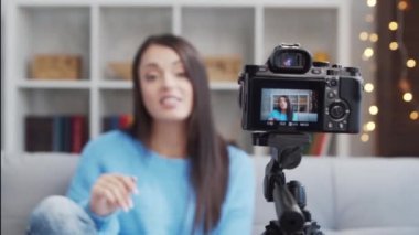 Genç ve çekici esmer kadın kamerayla video blogu kaydediyor. Mutlu kız evde oturuyor ve video kaydediyor..