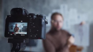 Genç moda video blogcusu kamera kullanarak kıyafet tasarımı hakkında video kaydediyor. Modern çatı katındaki iş yerinden yetenekli stilist akışı..