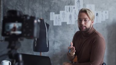 Genç moda video blogcusu kamera kullanarak kıyafet tasarımı hakkında video kaydediyor. Modern çatı katındaki iş yerinden yetenekli stilist akışı..
