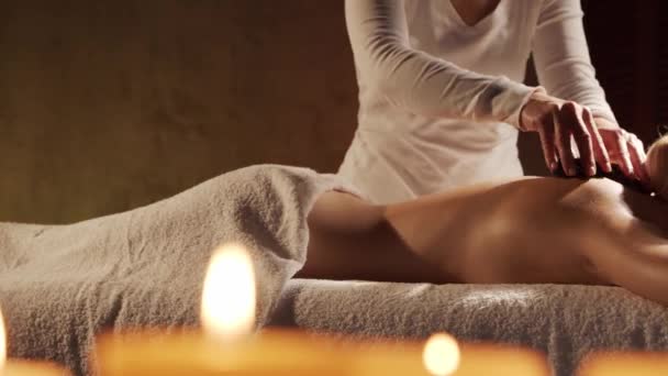 若く健康的で美しい女性は温泉サロンで熱い石マッサージ療法を取得します 健康的なライフスタイルとボディケアの概念 — ストック動画