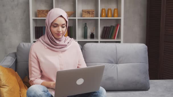 ヒジャーブ州の若く魅力的なイスラム教徒の女性は ラップトップコンピュータを使用して自宅で動作します 中東のフリーランスやソファの上の学生 ロックダウンの概念 — ストック動画