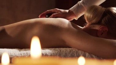 Genç, sağlıklı ve güzel bir kadın kaplıca salonunda sıcak taş masaj terapisi görüyor. Sağlıklı yaşam tarzı ve vücut bakımı kavramı.